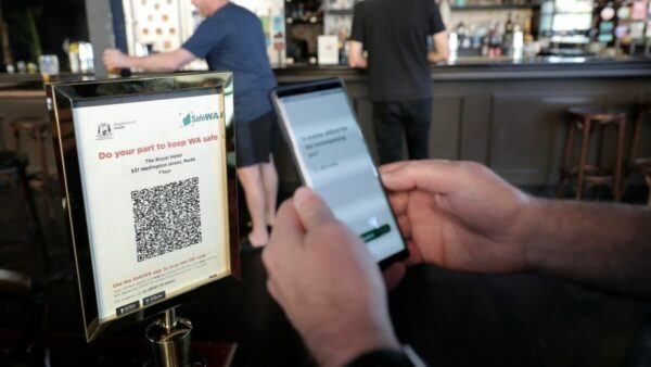 A person holds a phone up to a QR code at a cafe. The QR code says "do your part to be safe - SafeWA