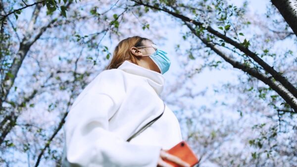 Woman walking through a park in spring with surgical mask and smartphone