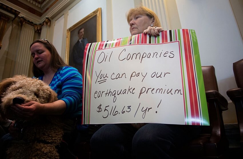 A women holds a sign reading "Oil companies YOU can pay our earthquake premium of $516.63/yr!"