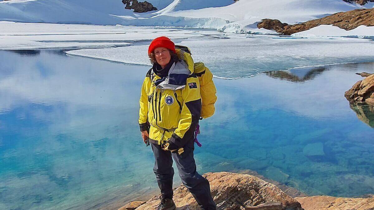 Person in bright yellow jacket stands on a rock in front of icy landscape