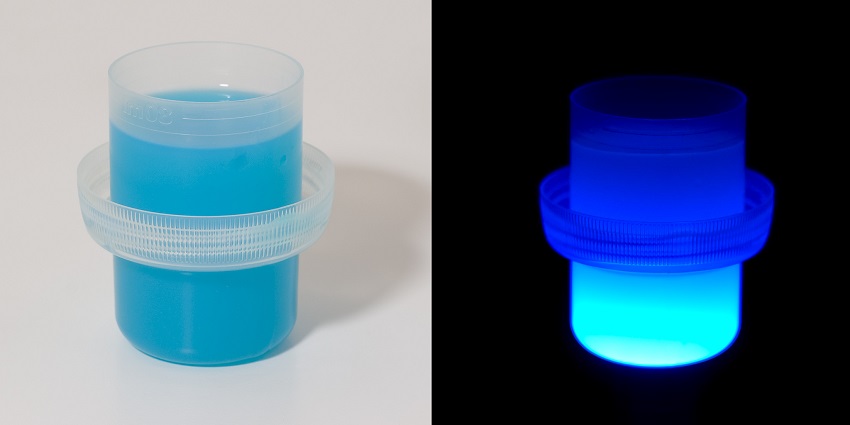 two photos of a cap of laundry liquid, one is well-lit and blue, one is glowing bright blue in the dark