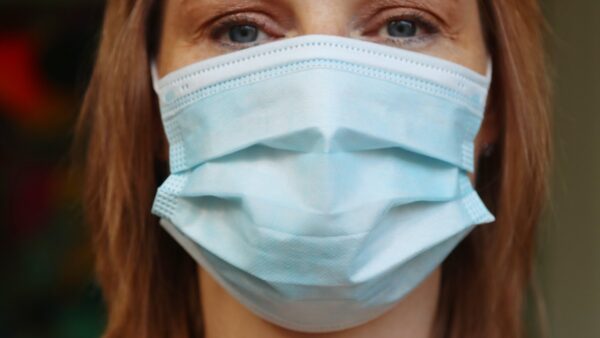 A woman with brown-red hair wears a blue surgical mask