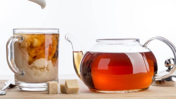 teapot filled with black tea next to mug with black tea and milk and sugar cubes