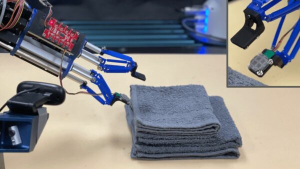 robot that can fold laundry: robotic arm with 2 pincers picking up a folded towel, inset in image shows coating on pincers in fine grey material