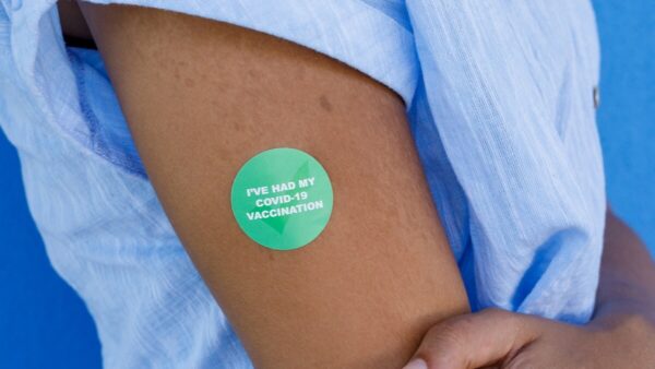 Person's arm with green Covid-vaccinated sticker