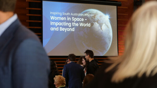 People in suits at an event with a powerpoint slide that says 'Inspiring South Australian Women, Women in Space - Impacting The World and Beyond