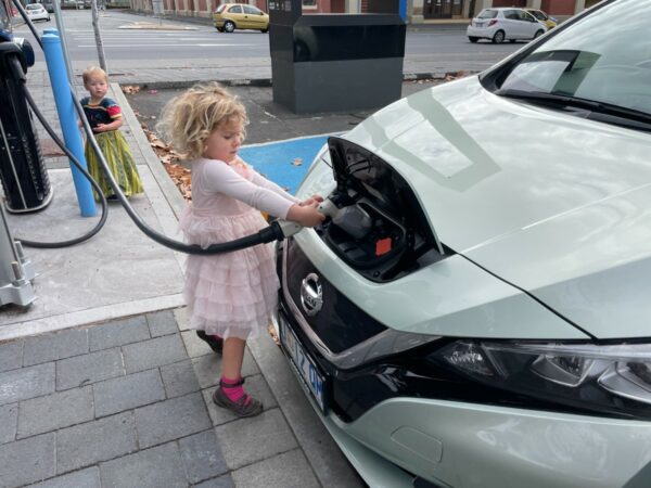 Child holds electric charging cable connected to vehicle