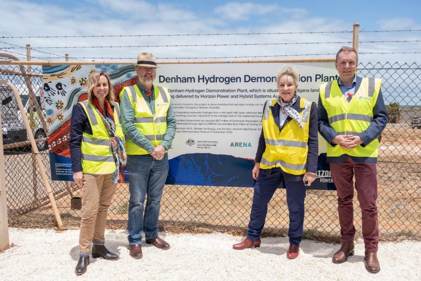 four people in high vis vests standing outside a fence with sign reading Denham Hydrogen Demonstration Plant