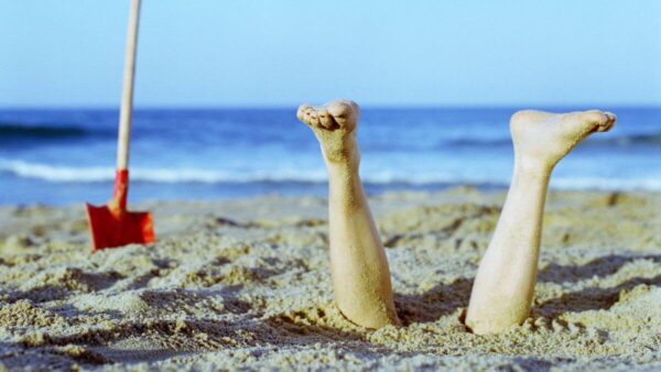 A woman's feet stick vertically out of the sand.