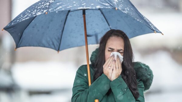 Woman holding umbrella sneezes into a handkerchief.