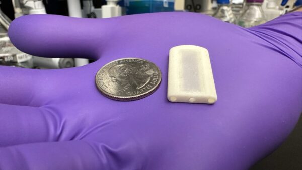 small white tablet next to coin on gloved hand