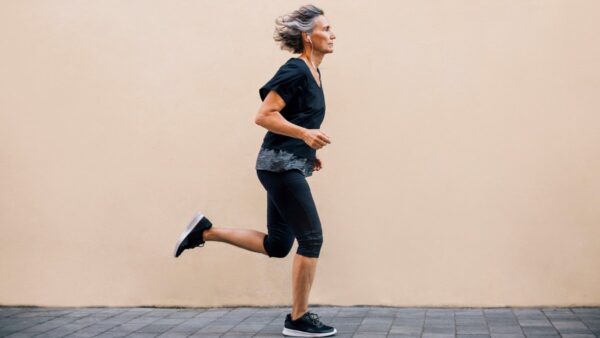 Side view of woman running on footpath against wall